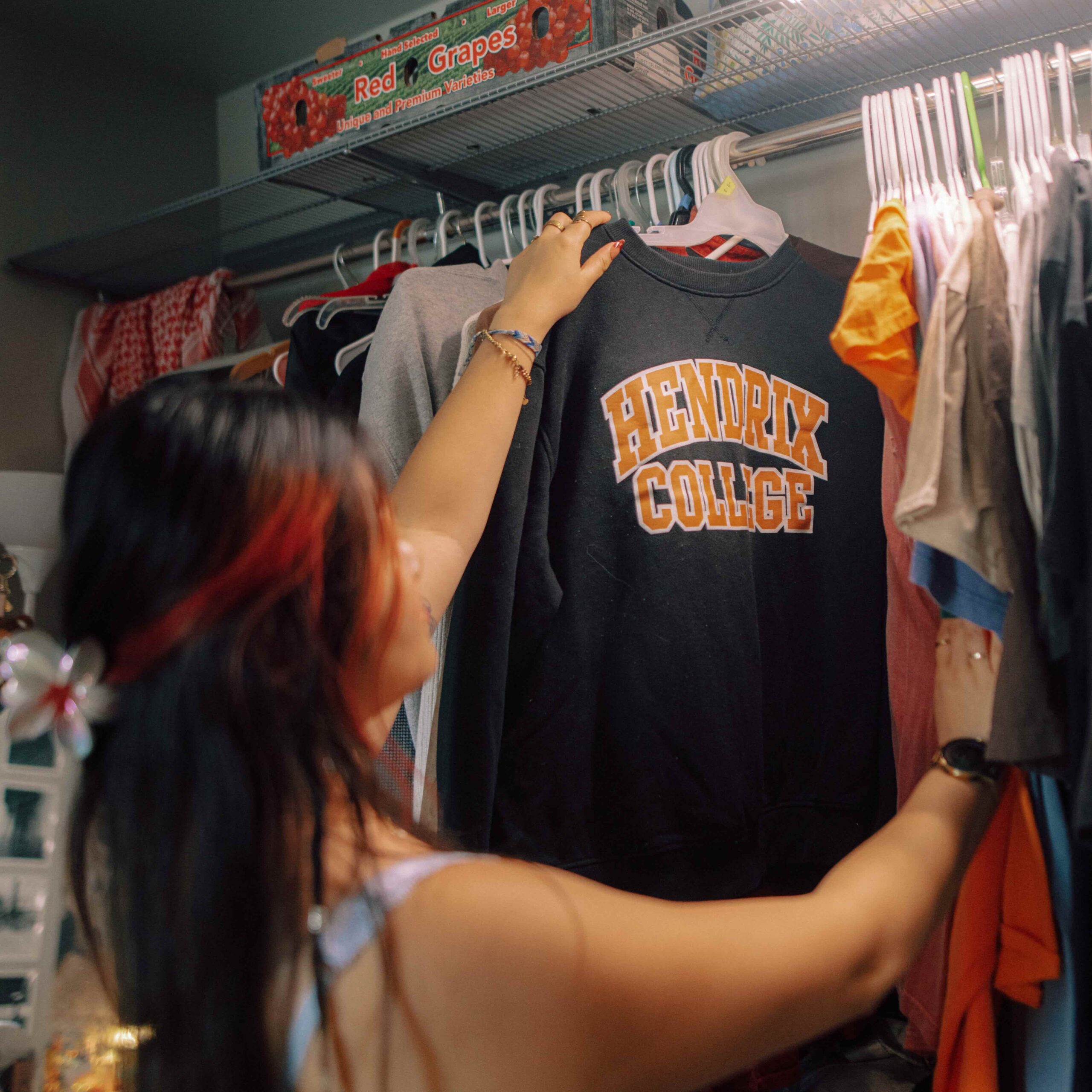 A student looking through clothes in a closet including a Hendrix College sweatshirt.
