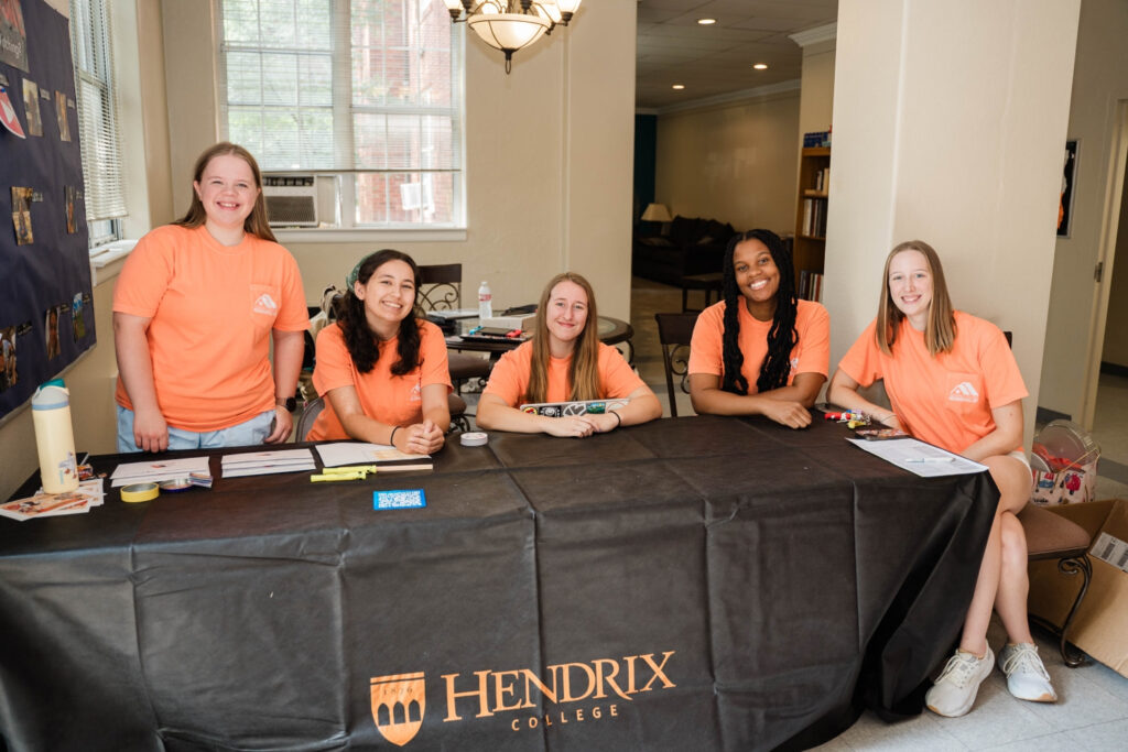 Five people sitting indoors behind a black Hendrix-branded table smiling at the camera.