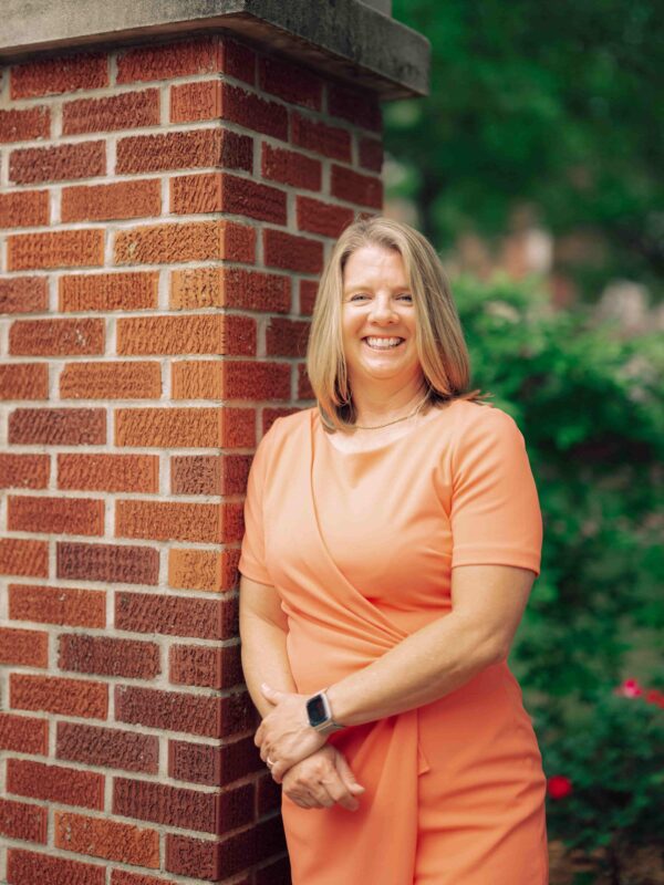 President Karen Petersen smiles and leans on a brick column with hands crossed.