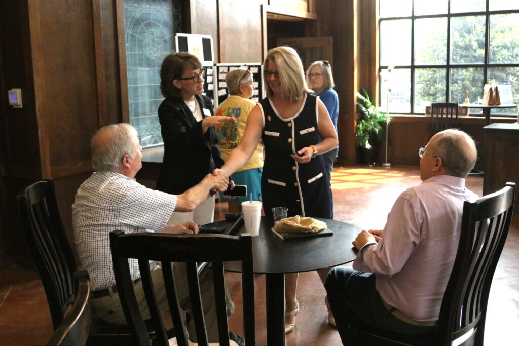 President Petersen shakes hands with a seated person while another seated person looks on.
