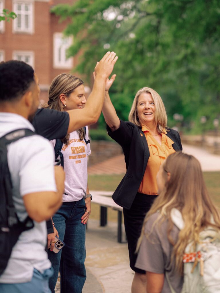 President Karen Petersen gives a high five to a student while two other students look on.