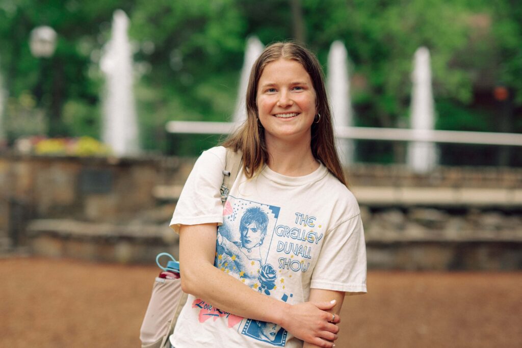 A smiling student standing outside on campus, with fountains in the background.