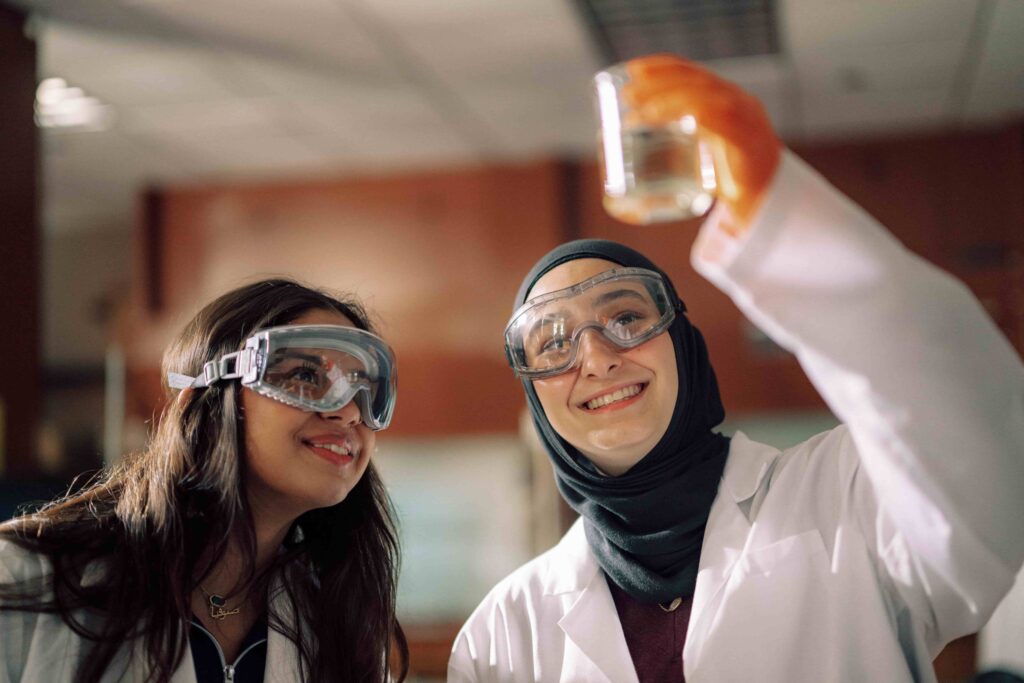 Two students wearing safety goggles looking at the contents of a jar while doing an experiment.