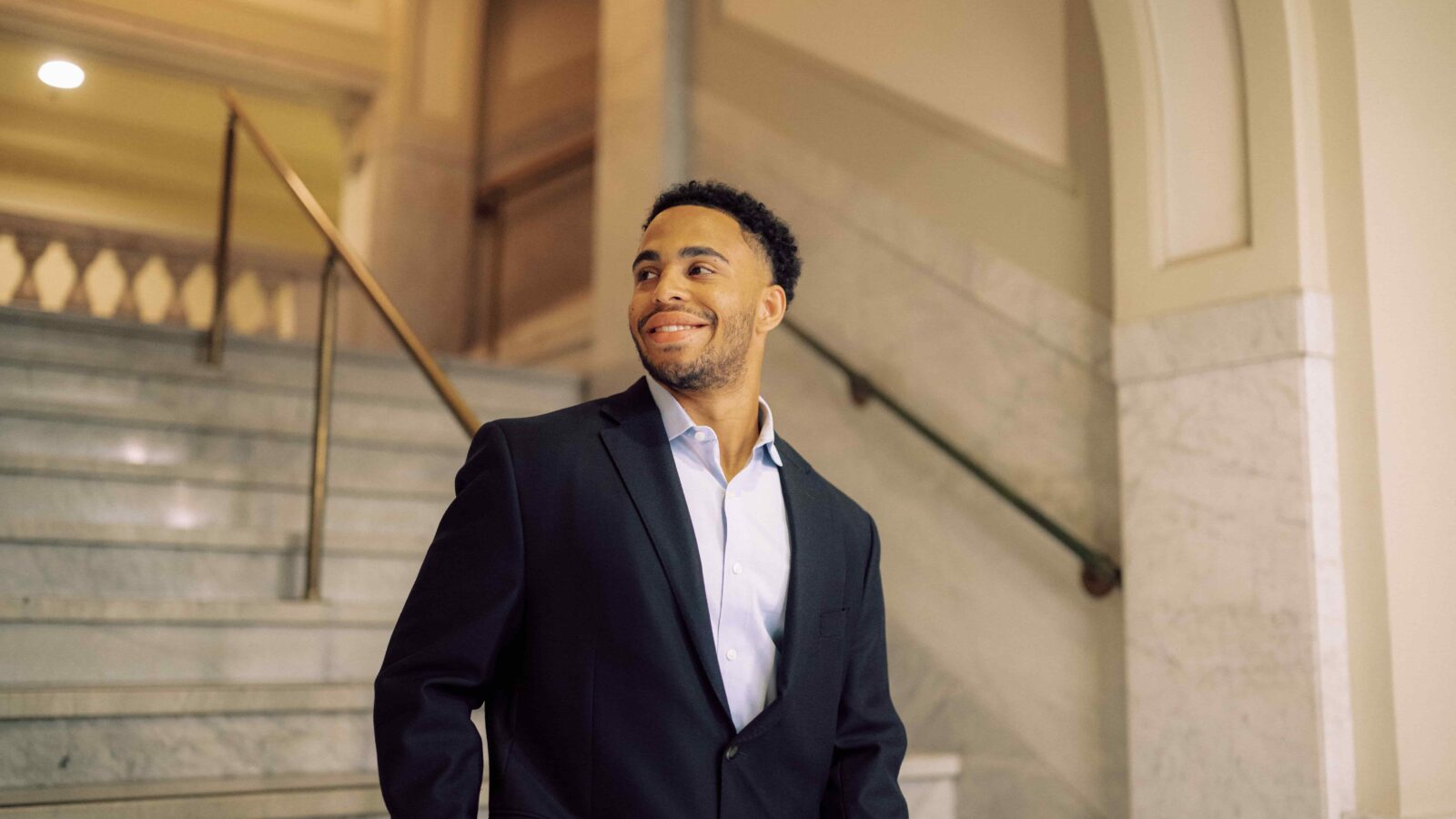 A man in a suit standing on marble steps inside a building.