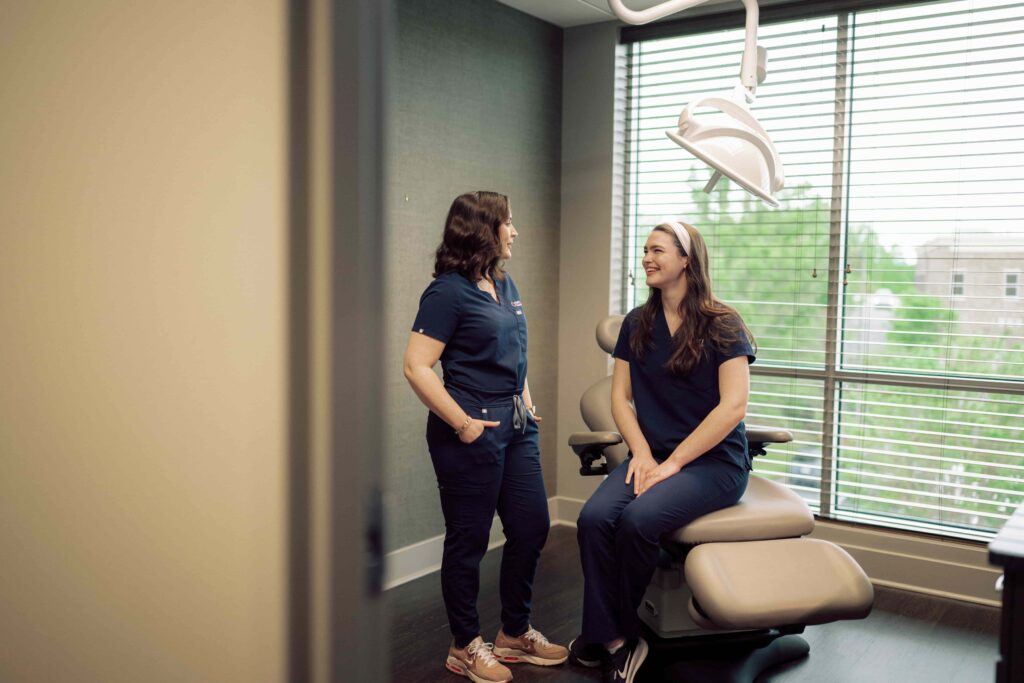 Two students in medical scrubs having a conversation in a patient exam room.