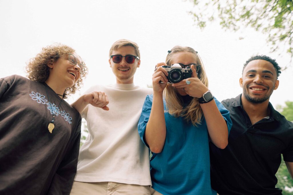 Four smiling students standing shoulder to shoulder, one student is holding a camera.