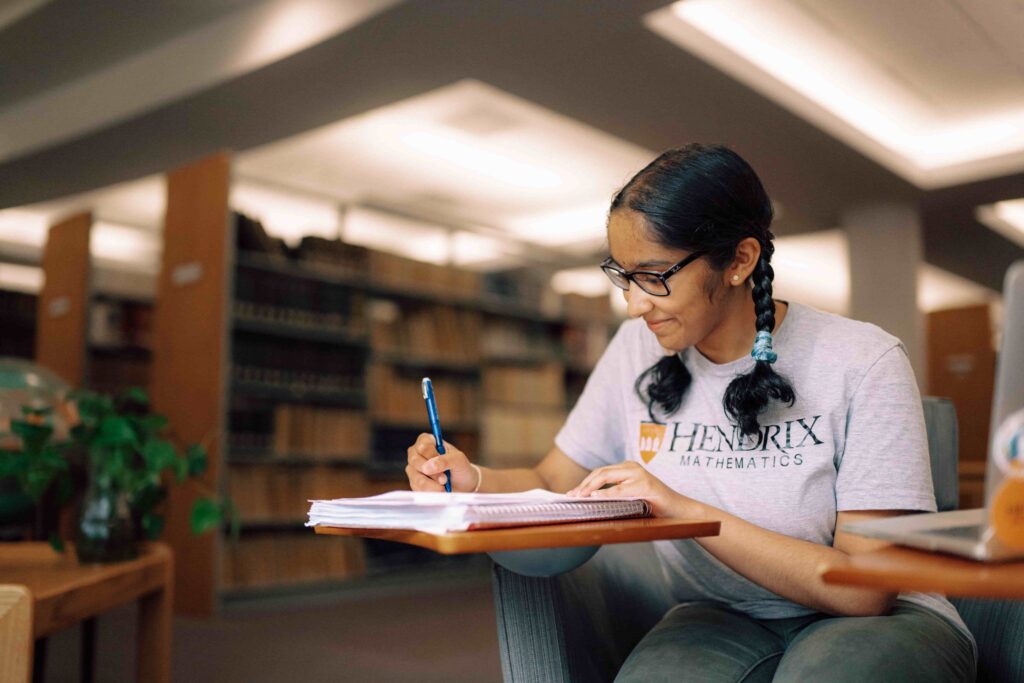A student sitting in the library, writing in a notebook.
