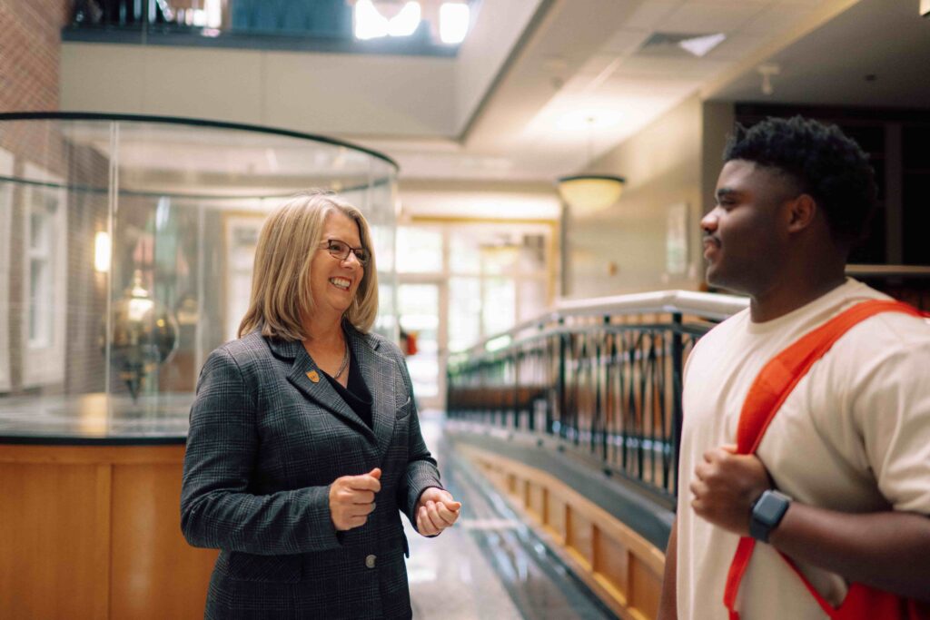 President Petersen speaking with a student in the lobby of a building on campus.