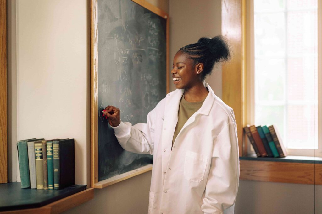 A smiling student writing chemical equations on a chalkboard.