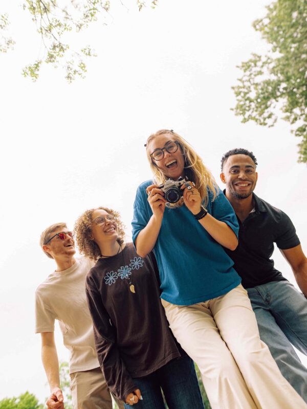 Four laughing students huddled together, one student is holding a camera.