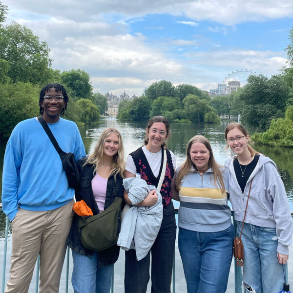 Five Hendrix students stand next to each other on a sunny day in London, England. Behind the students are trees, buildings, and a ferris wheel.