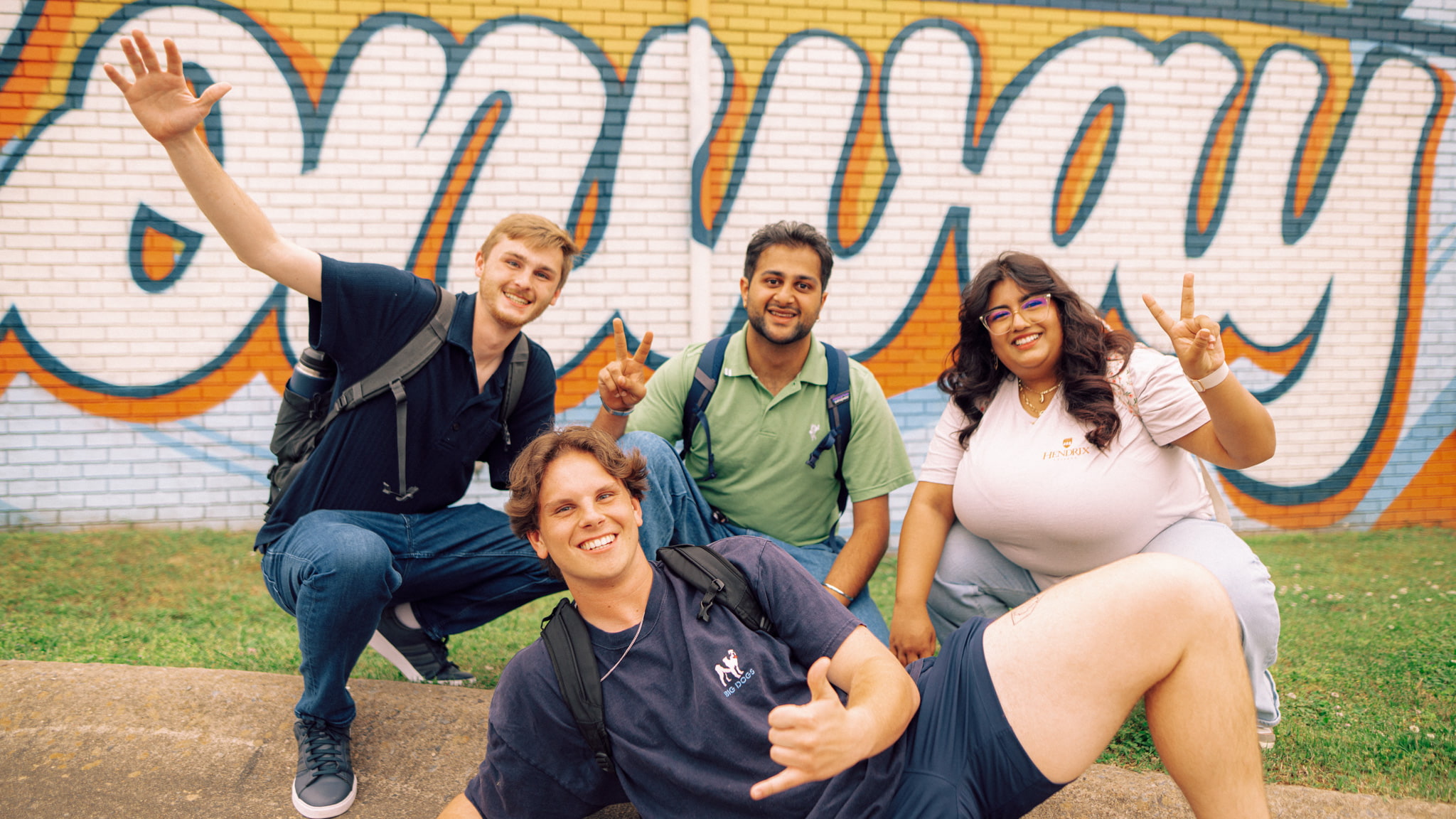 Four people sit and smile in front of the “We love Conway” mural.