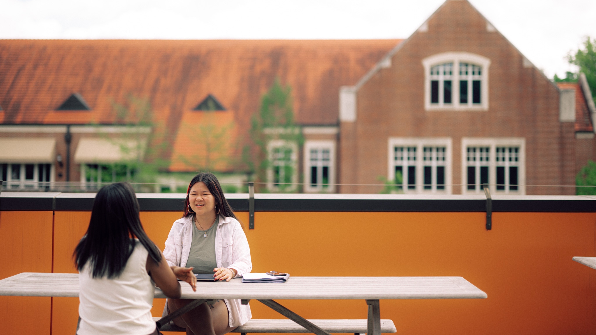 Two people sitting at a table outside in front of a red bricked building.