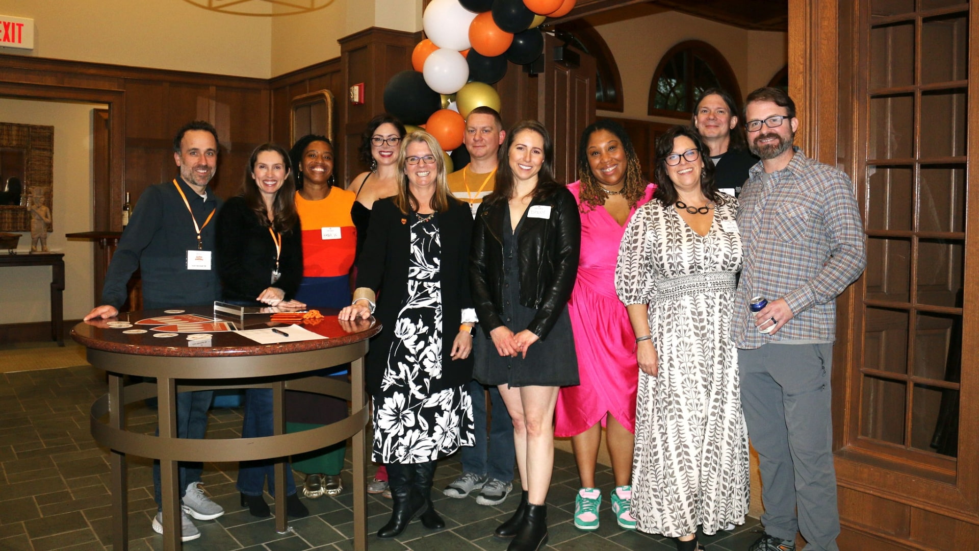 The Hendrix President, Karen Petersen, stands with alumni celebrating an event in a well-lit room with balloons behind them.