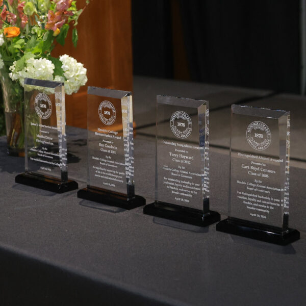 Four glass awards sit on a table with a vase of flowers near them.