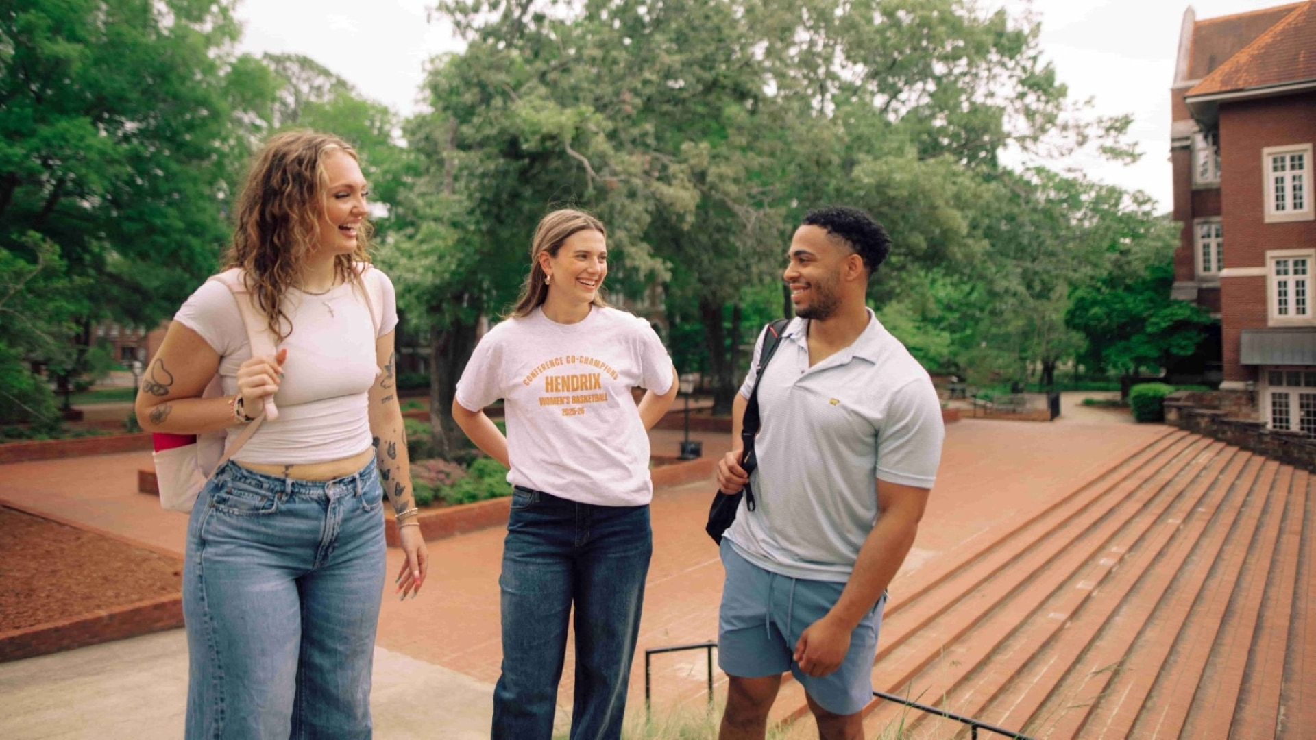 Three students chatting outdoors near a set of stairs.