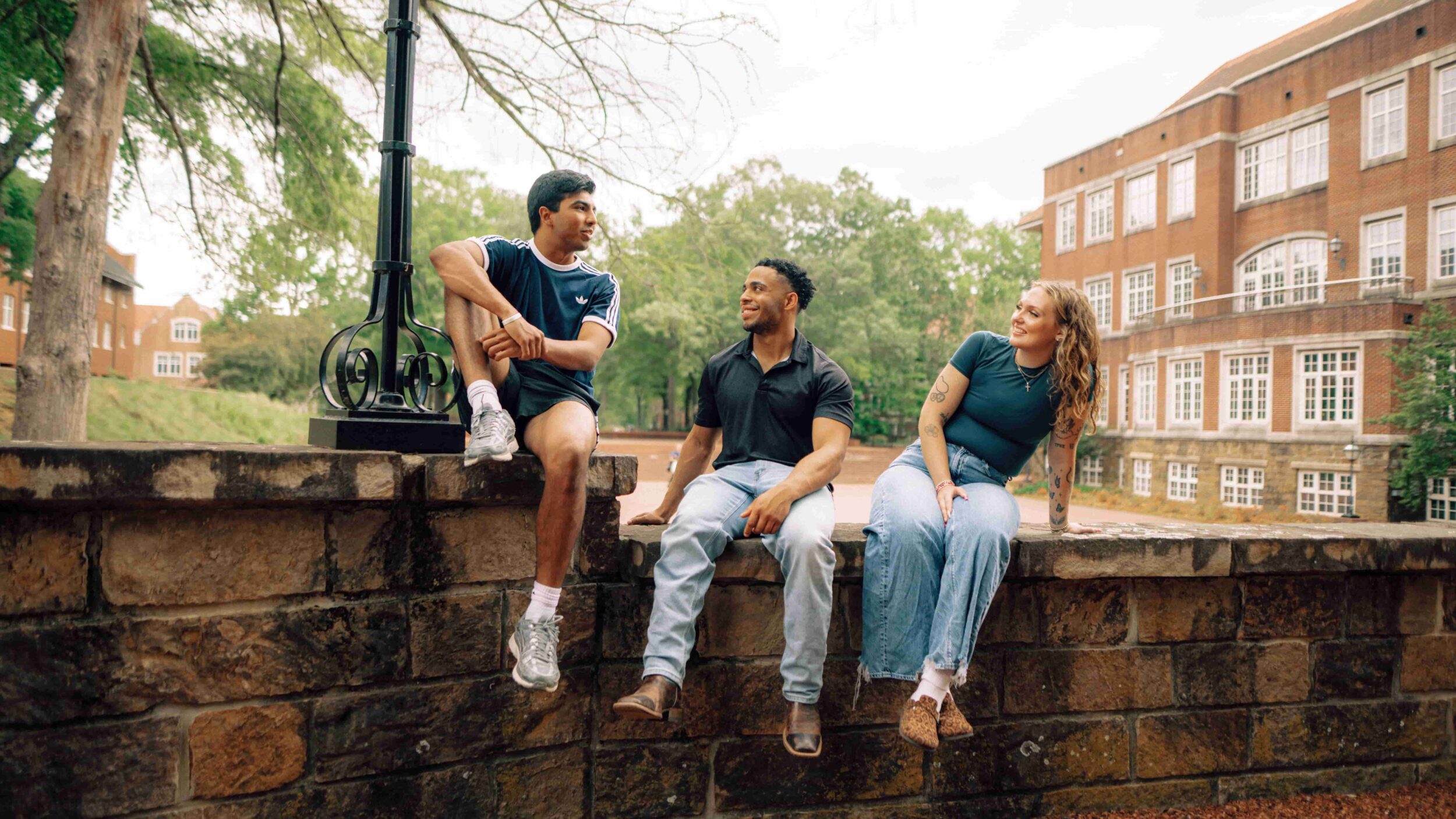 Three students sit together on a brick wall.