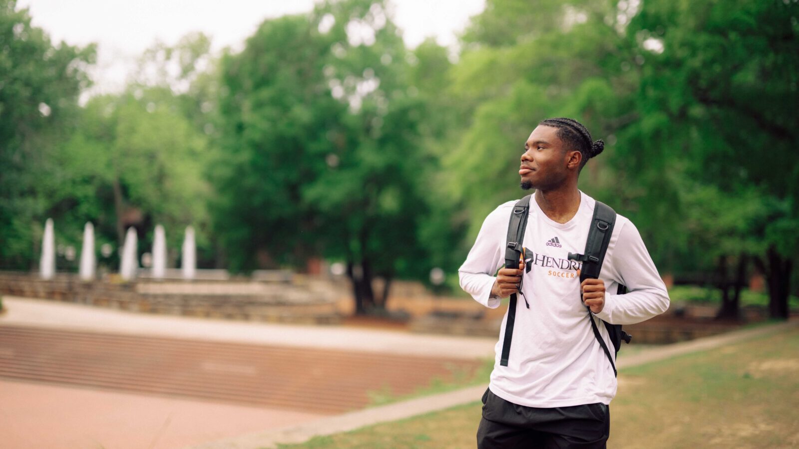 Student wearing a backpack is looking off to the side with the Hendrix College campus in the background.