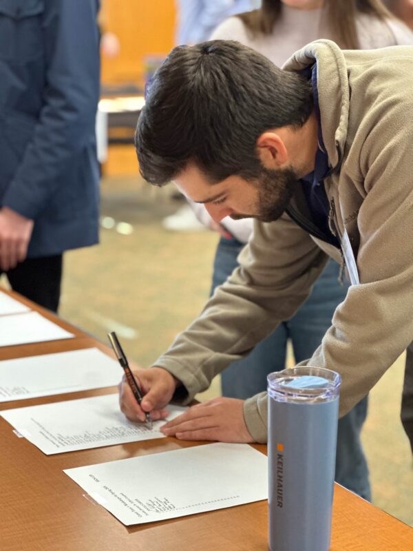 A student leans over to write on a sheet of paper that is on a table.