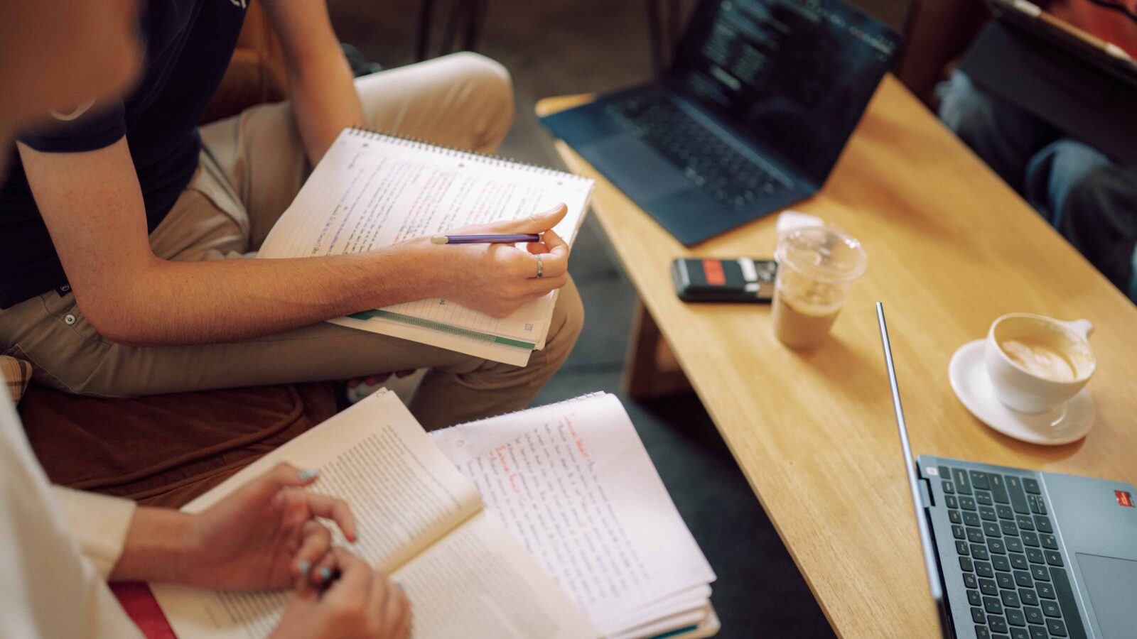 Students sitting at a table with notebooks and devices.