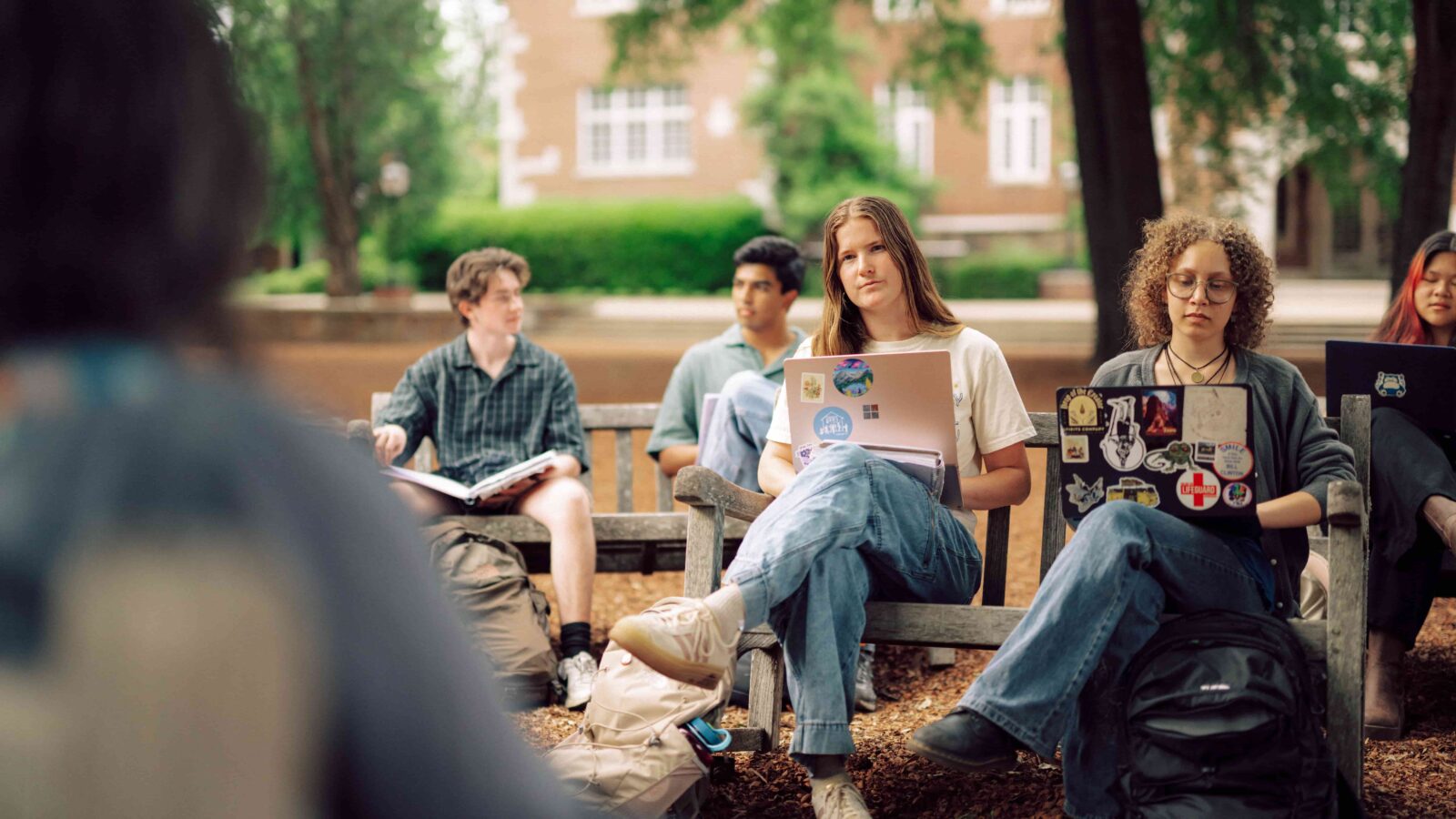A group of students with devices sitting outdoors on benches while having class.