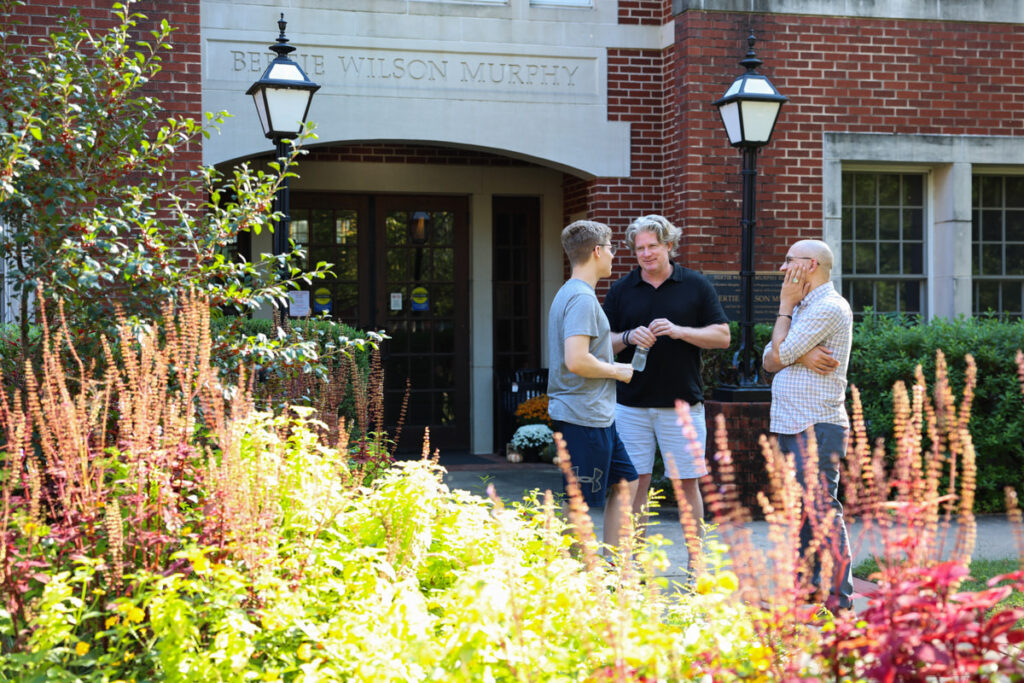 A student speaking with two faculty members near the entrance to a building on the Hendrix College campus.