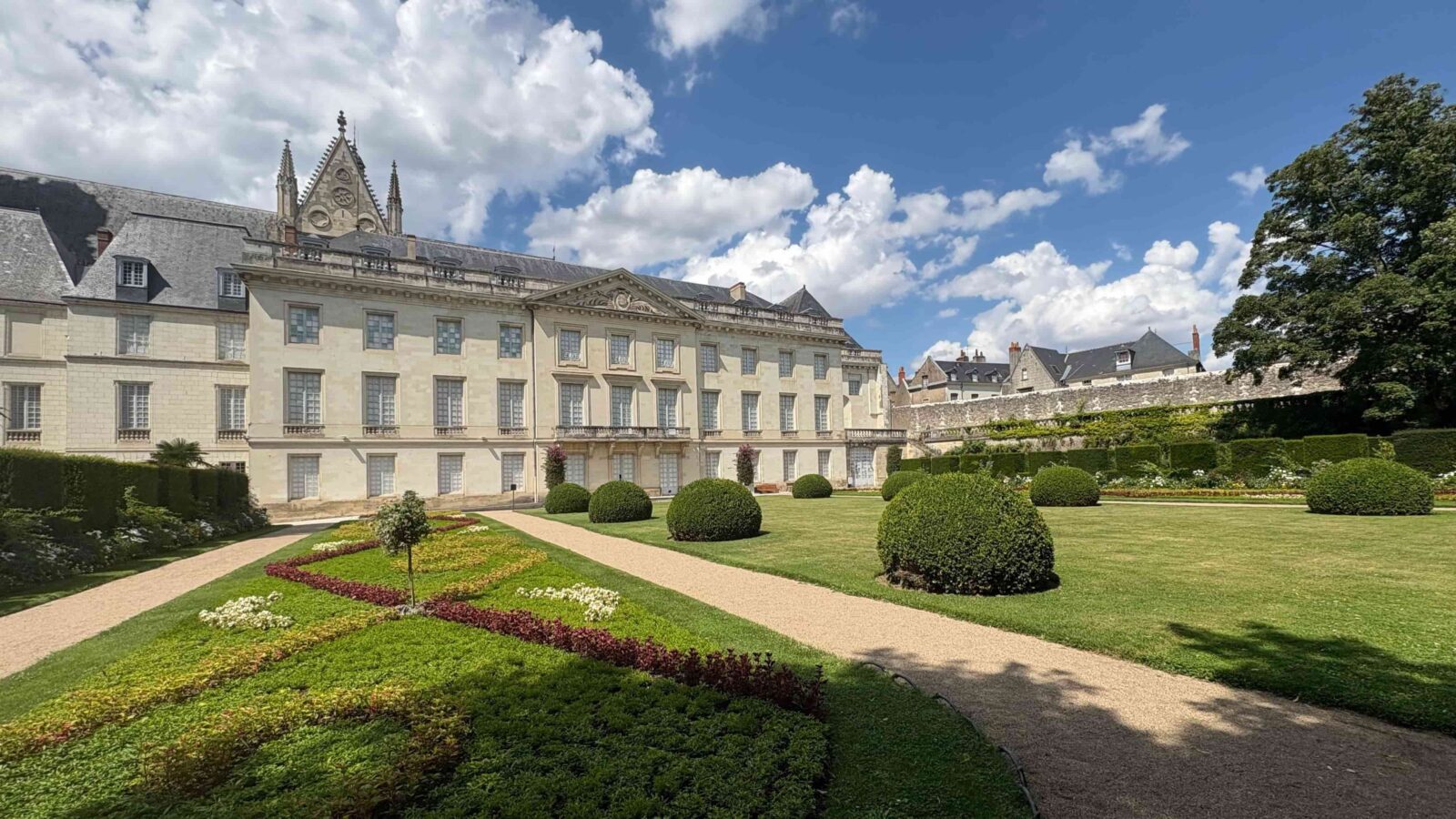 A large building in French architecture on a sunny day with manicured gardens.