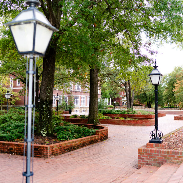 Two lamps at Hendrix College with a red brick sidewalk and trees surrounding them.