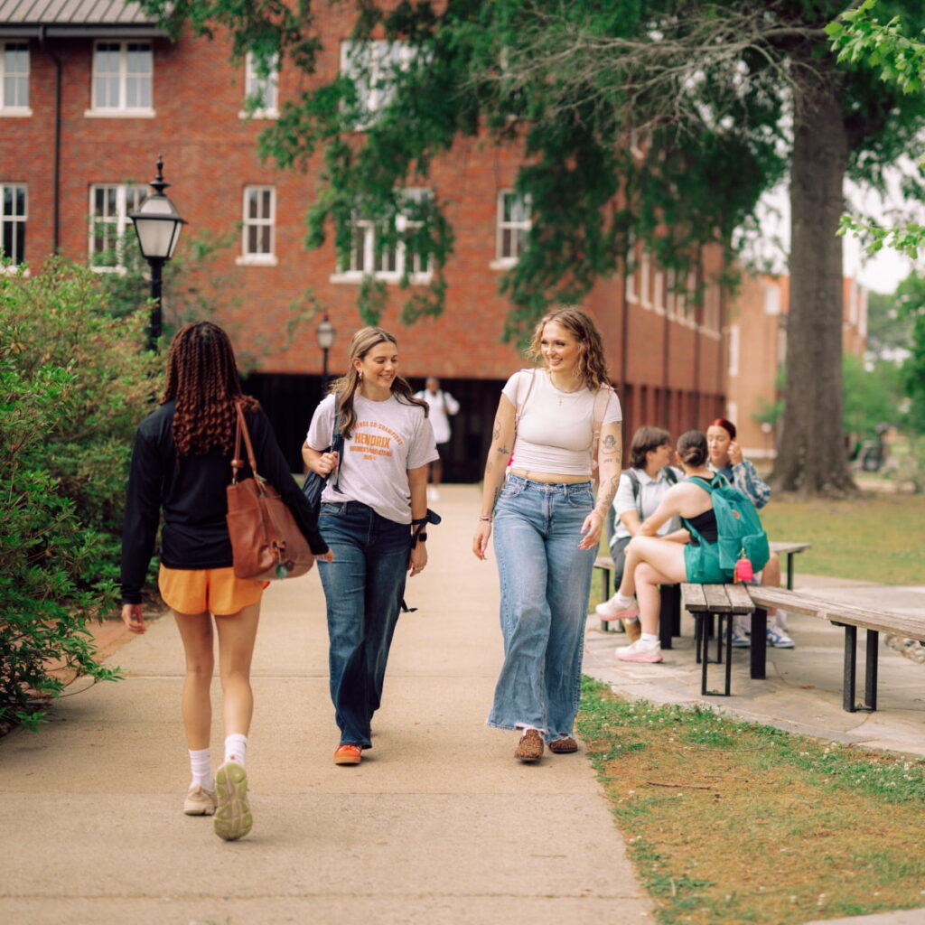 Three students gather on outside benches while four students walk beside them on the sidewalk at Hendrix.