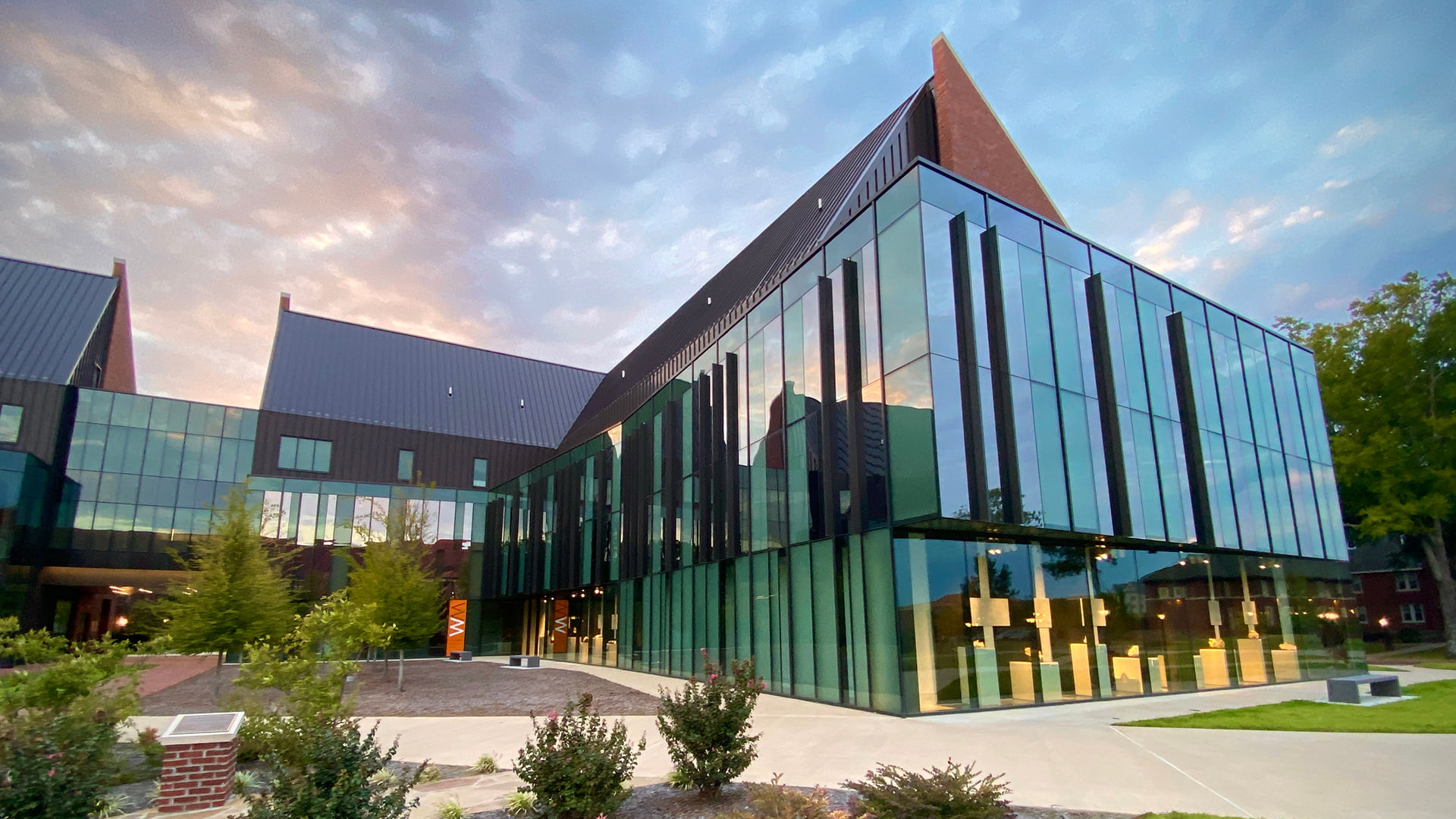 A glass-paneled building with a slanted rooftop, known as the Windgate Museum of Art, reflecting a cloudy day at Hendrix College.