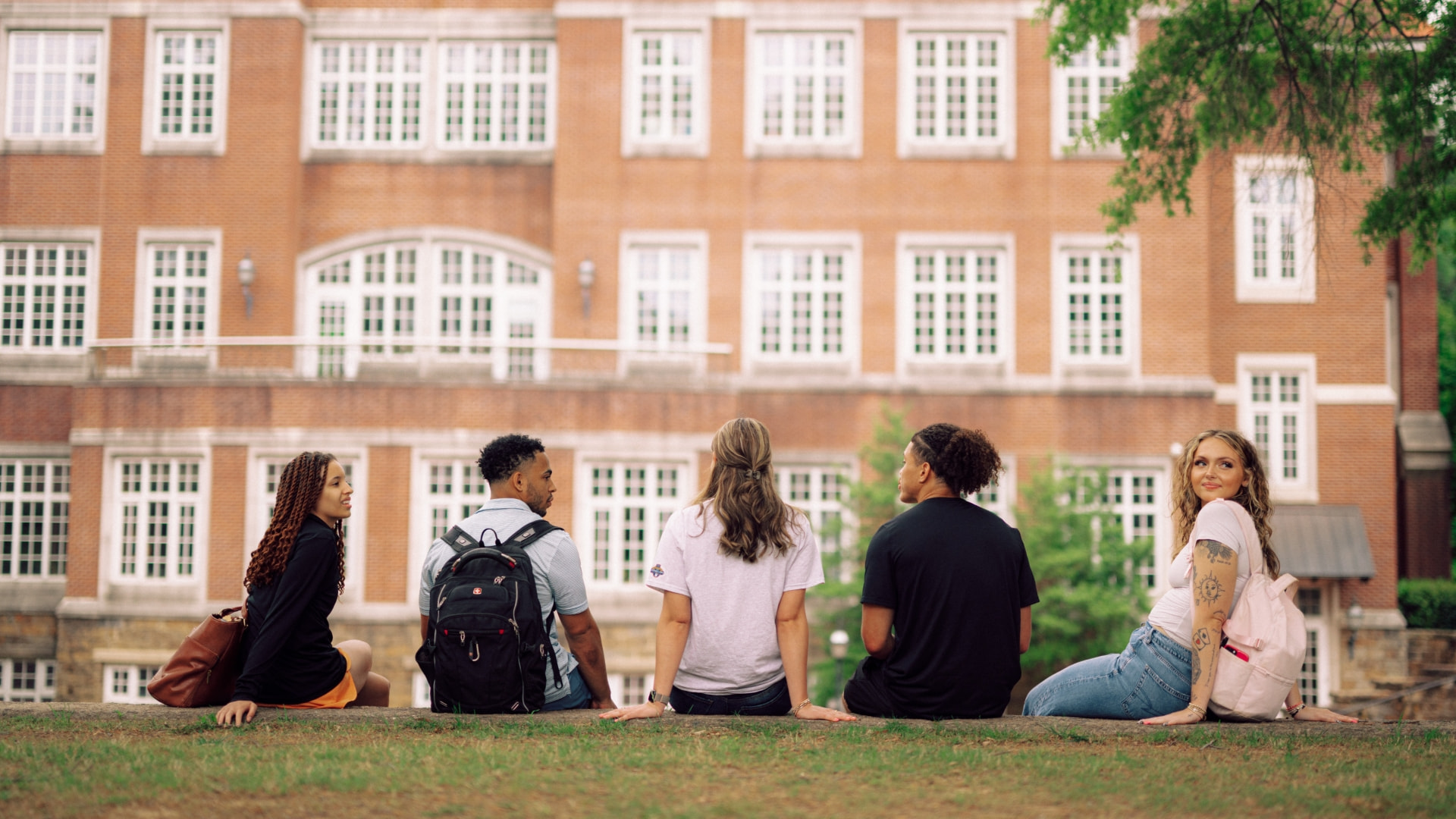 Five students sitting outdoors on a grassy hill.