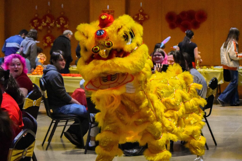 A dragon puppet walks between tables of students.
