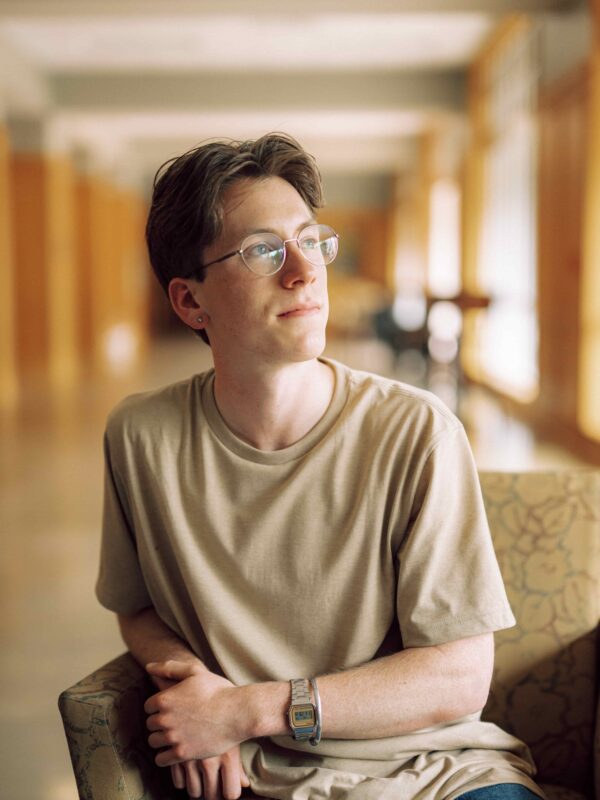 A student sitting indoors looking outdoors through some windows.
