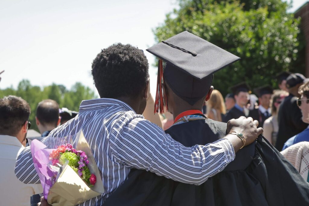 A student wearing regalia at commencement celebrating with friends.