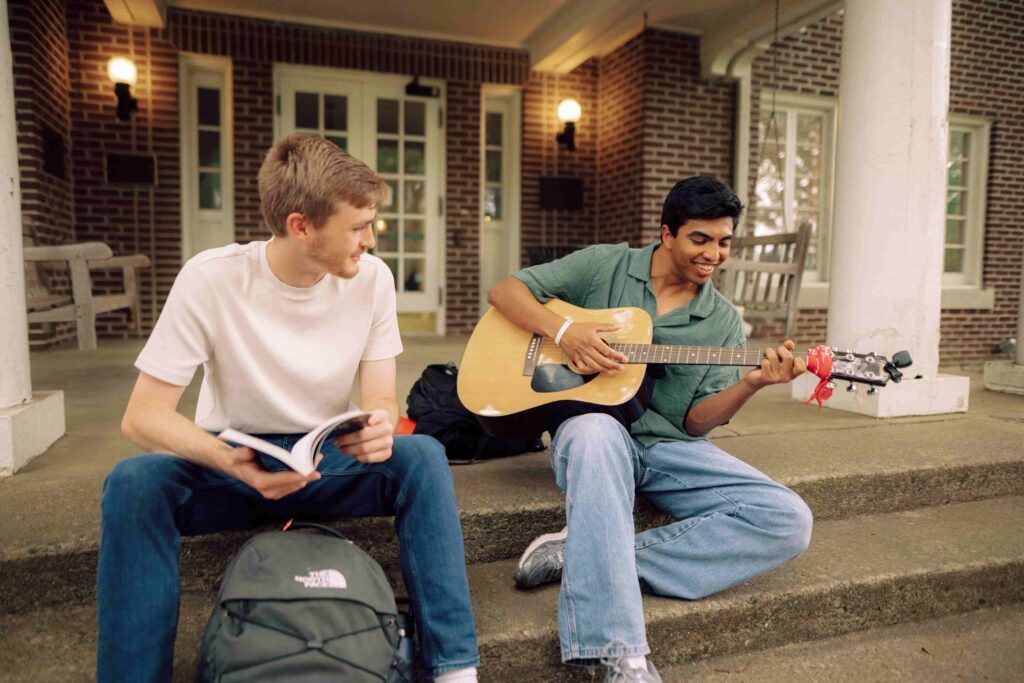 Students sit on the porch of Ellis Hall while one plays a guitar.