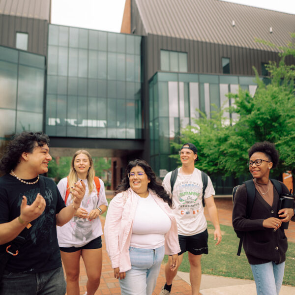 Five Hendrix students walking side by side, chatting, with a glass-paneled building behind them.