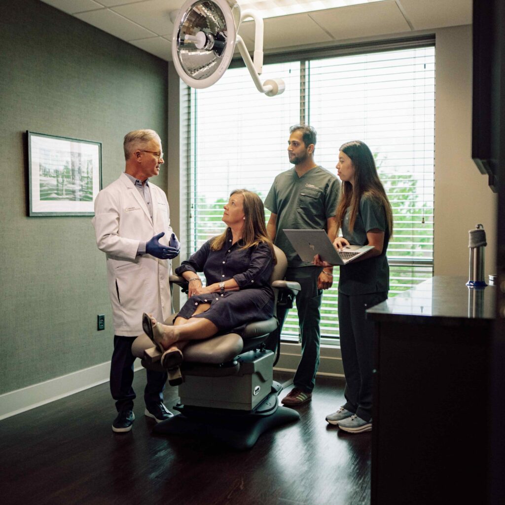 A dentist speaks to a patient and two students.