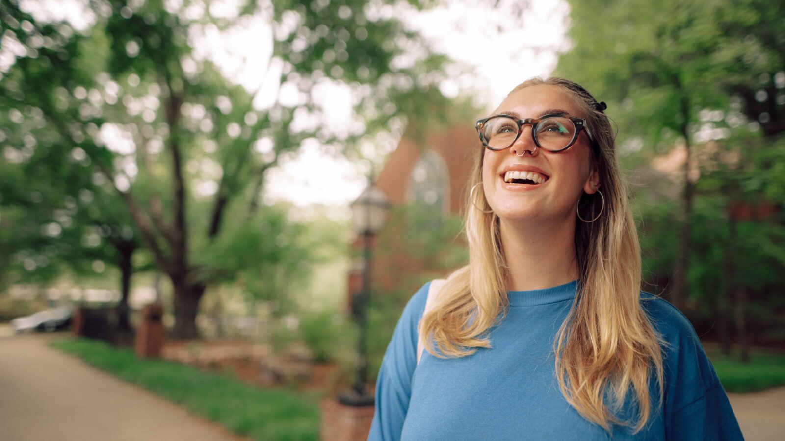 A smiling student stands outdoors near trees.