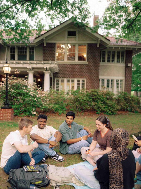 A group of students sits together on the grass under a tree.