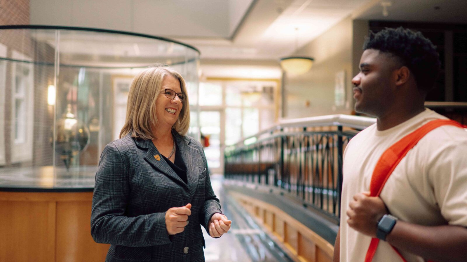 A student and mentor stand talking in an academic building.