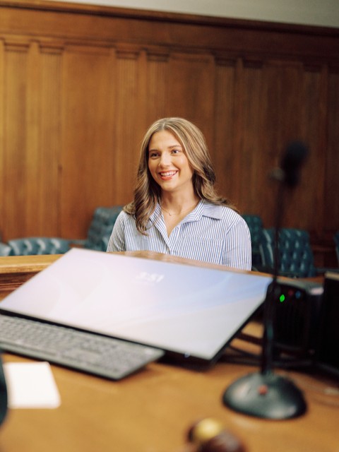 A student stands near a judge's bench in a courtroom.