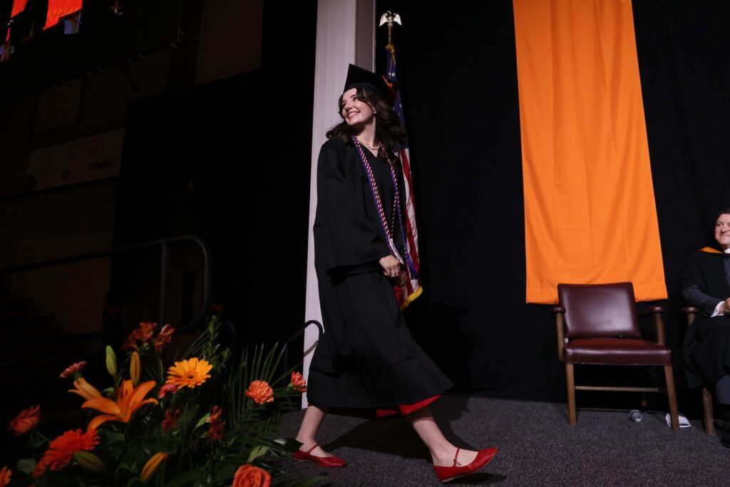A student smiles while crossing the stage at commencement.