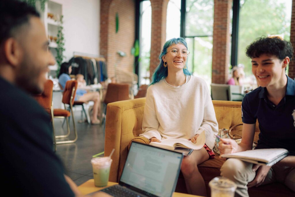 Smiling students gather at a coffee shop to study.