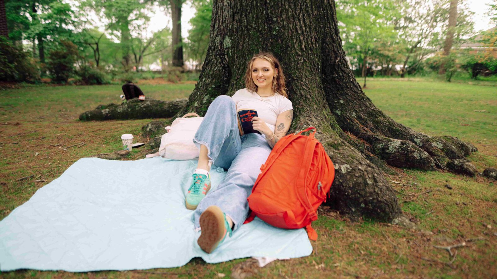 A student reclines against a tree with books.