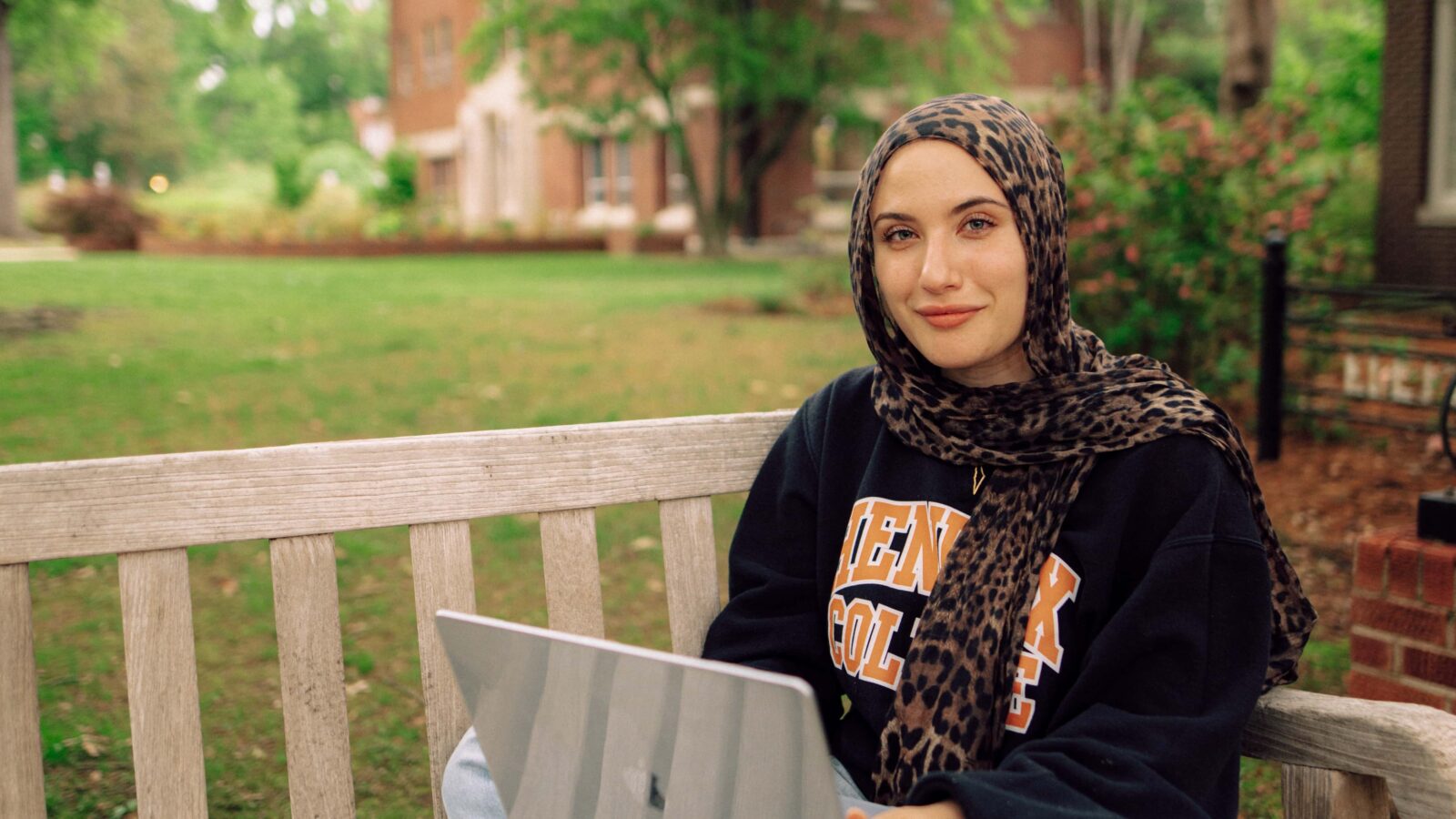 A student sits on a bench outdoors with a laptop computer.