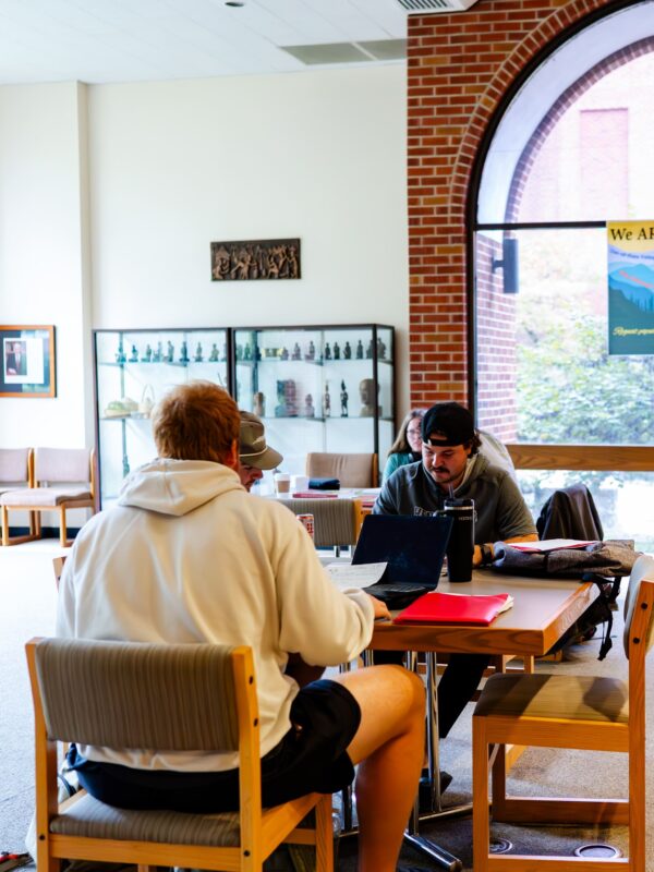 A group of students sit together at a table in a library.