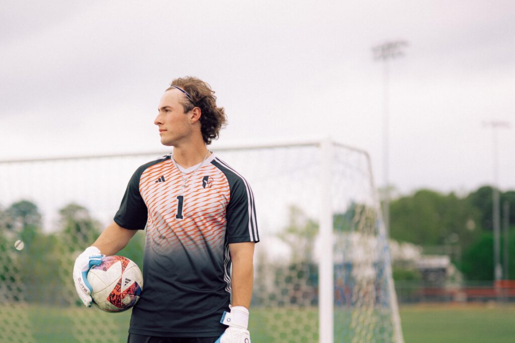 A soccer goalie stands on the field with a ball.