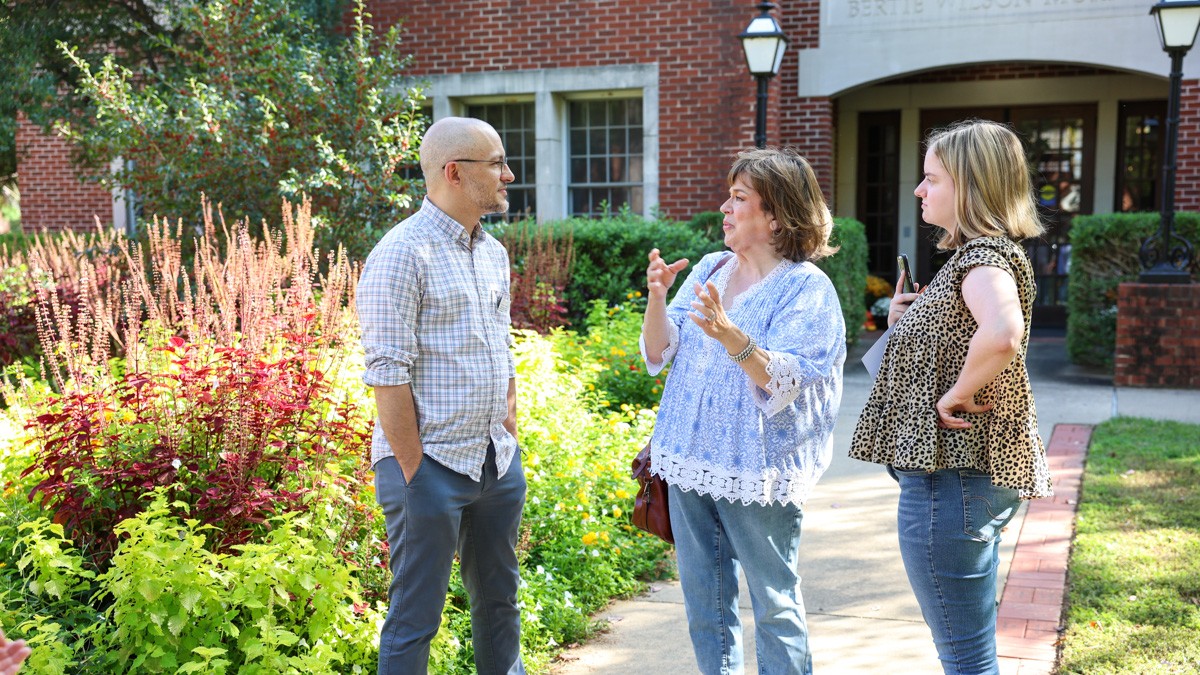 A group of adults stand together outside while having a conversation.