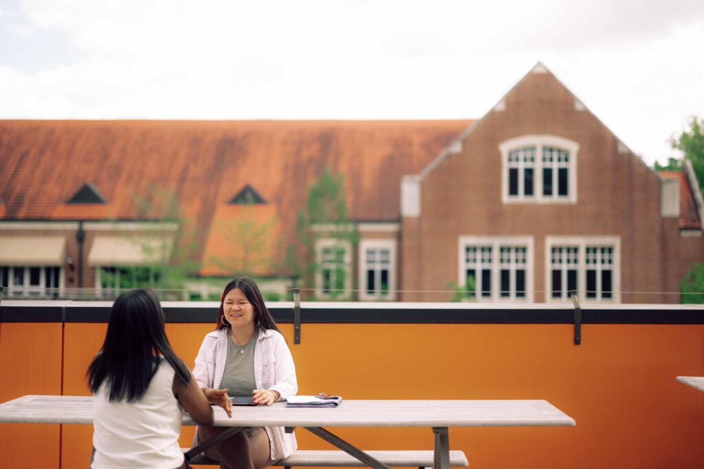 Two students having a conversation at an outdoor table.